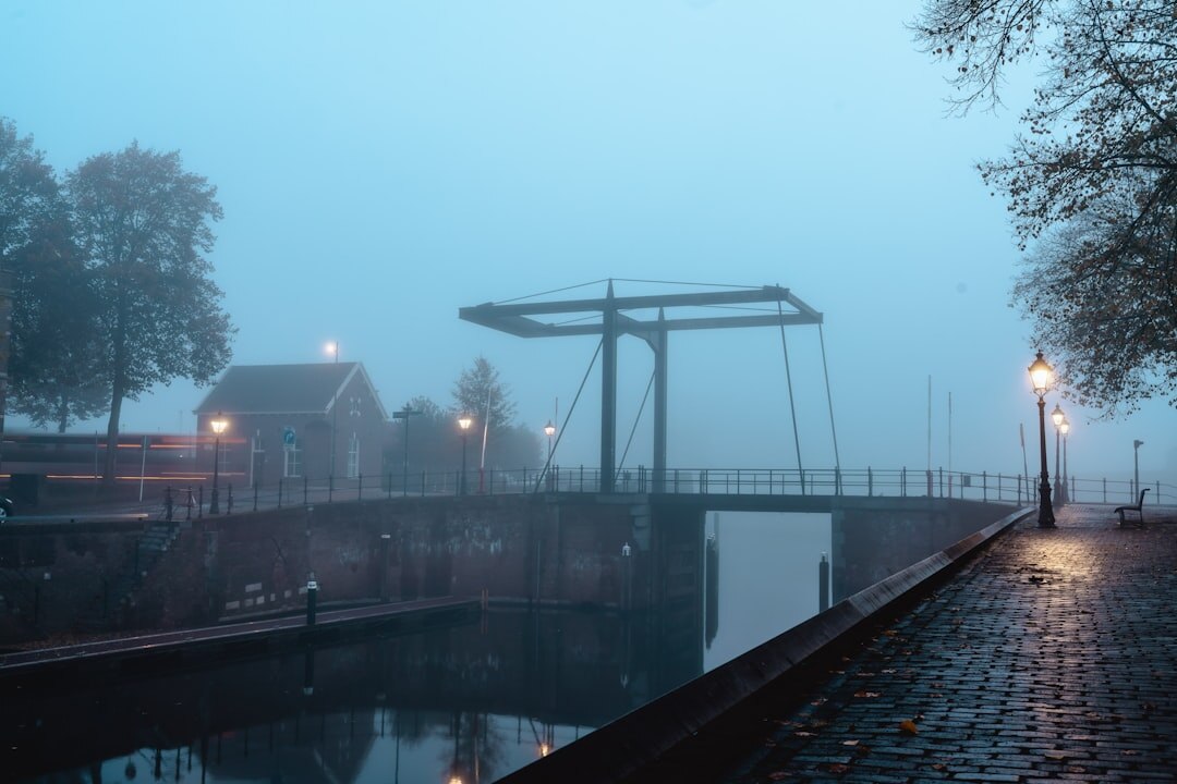 Foggy Dutch canal at dawn with silhouetted figure walking on the bridge